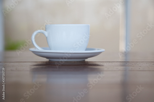 A white cup of coffee placed on a wooden table by the window in a coffee shop, Concept: Delicious breakfast drinks fragrant suitable for lifestyle, closeup cup of coffee over the top with space