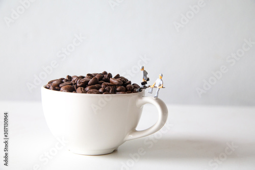 miniature people standing on a white coffee cup with brown coffee beans  Concept  teamwork professionalism and beverage business ideas successful  close-up macro toy small creative lifestyle