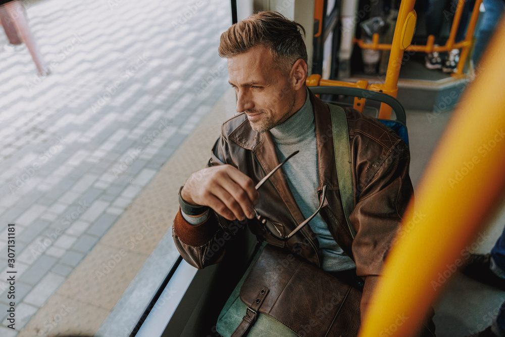 Good-looking man sitting in tram and looking out of the window