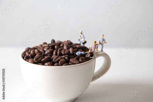 miniature people standing on a white coffee cup with brown coffee beans  Concept  teamwork professionalism and beverage business ideas successful  close-up macro toy small creative lifestyle