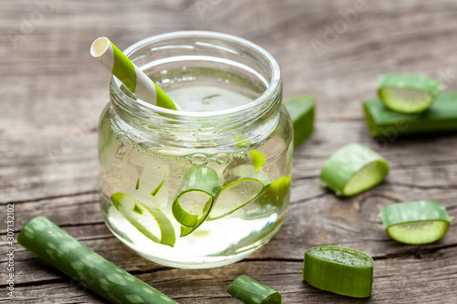 Aloe Vera green cocktail for healthy body and body. Aloe pulp slices in a glass jar and leaves on a wooden table
