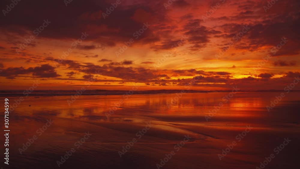 Beautiful sunset on a wide and remote sandy Pacific beach at Manuel Antonio National Park, Costa Rica. The clouds are colorizing the entire sky and the waves. A baby turtle is moving toward the water.