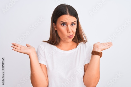 Portrait of beautiful and young brunette woman standing over isolated white background clueless and confused expression with arms and hands raised. Doubt concept.