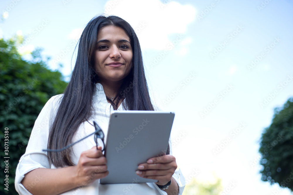 portrait of an indian girl. Business lady holding glasses and tablet in her hands. Outdoors portrait of an indian girl. Business lady holding glasses and tablet in her hands. Outdoors