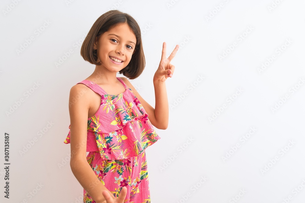 Young beautiful child girl wearing pink floral dress standing over isolated white background smiling looking to the camera showing fingers doing victory sign. Number two. Young beautiful child girl wearing pink floral dress standing over isolated white background smiling looking to the camera showing fingers doing victory sign. Number two.