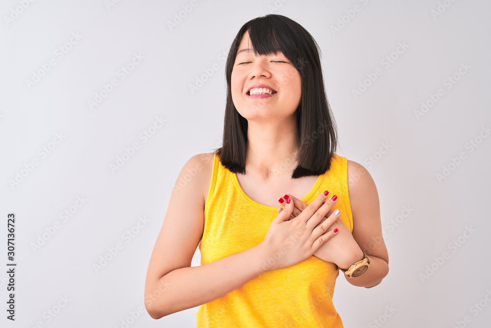 Young beautiful chinese woman wearing yellow t-shirt over isolated white background smiling with hands on chest with closed eyes and grateful gesture on face. Health concept.