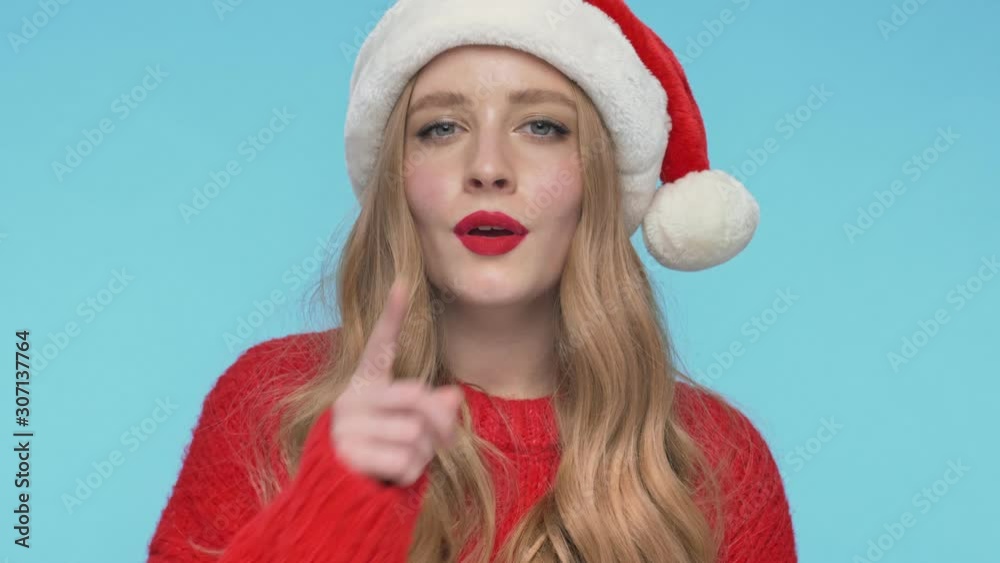 Close up view of Cheerful mystery pretty woman in christmas hat having secret and showing silence gesture over turquoise background Close up view of Cheerful mystery pretty woman in christmas hat having secret and showing silence gesture over turquoise background