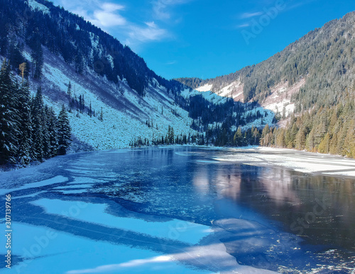 Frozen partially shaded Talapus Lake of the Alpine Lake Wilderness on a snow covered day with Cedars and Hemlock trees on the mountain side in Washington State.