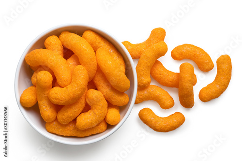 Extruded cheese puffs in a white ceramic bowl next to spilled cheese puffs isolated on white. Top view. photo