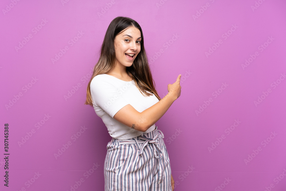 Young woman over isolated purple background pointing back Young woman over isolated purple background pointing back