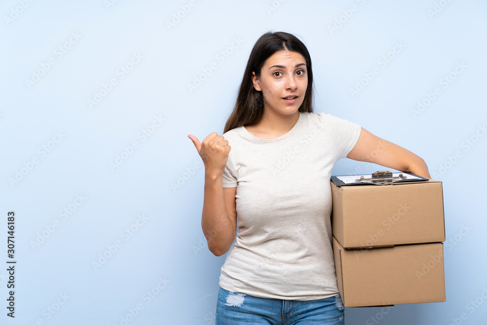 Young delivery woman over blue brick wall pointing to the side to present a product Young delivery woman over blue brick wall pointing to the side to present a product
