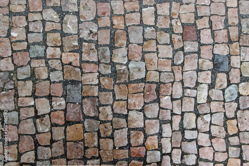 An old damaged stoneblock pavement cobbled with small stone blocks of different colors