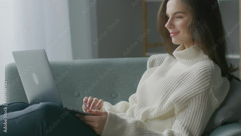 Beautiful Young Woman Works on Laptop Computer while Sitting on the Chair. Sensual Girl Wearing Sweater Works On Notebook; Studies, Surfs Internet, Uses Social Media while Relaxing in Cozy Apartment Beautiful Young Woman Works on Laptop Computer while Sitting on the Chair. Sensual Girl Wearing Sweater Works On Notebook; Studies, Surfs Internet, Uses Social Media while Relaxing in Cozy Apartment