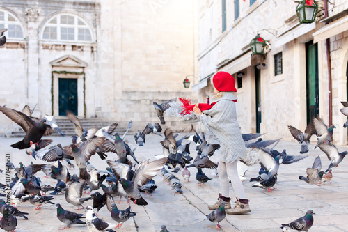 Christmas mood and holidays in Europe. Child girl feeds doves on square. Pigeons flying around cute kid. Romantic vintage atmosphere in old town in Italy. Authentic, ancient architecture.