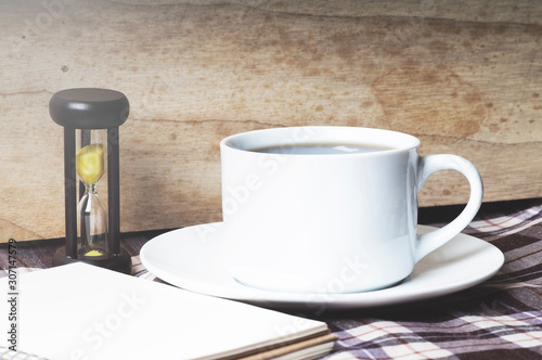 Coffee Break. Cup of coffee with notebook, Hourglasses on wooden background