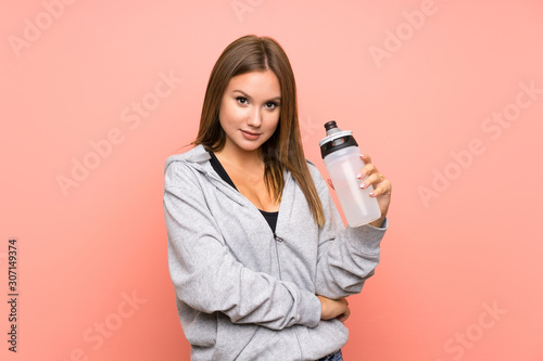 Teenager sport girl with a bottle of water over isolated pink background