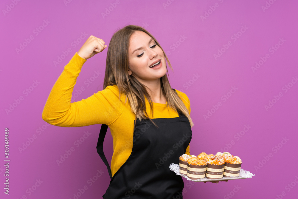 Teenager girl holding lots of different mini cakes over isolated purple background celebrating a victory Teenager girl holding lots of different mini cakes over isolated purple background celebrating a victory