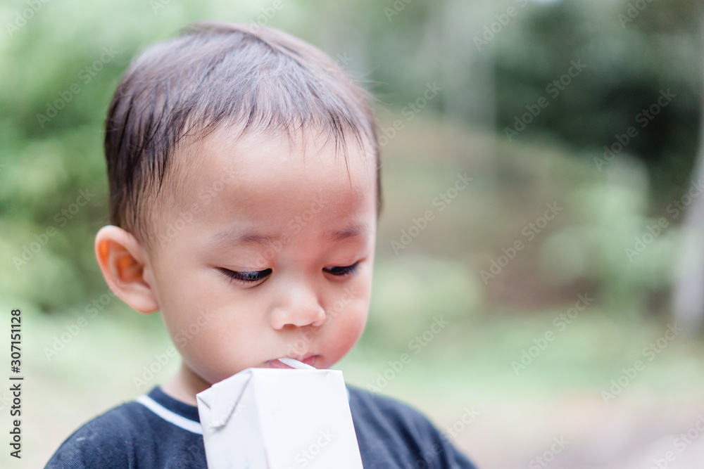 Closeup of little toddler boy drinking milk box with straw in the park.Happy toddler baby boy hungry milk. Closeup of little toddler boy drinking milk box with straw in the park.Happy toddler baby boy hungry milk.