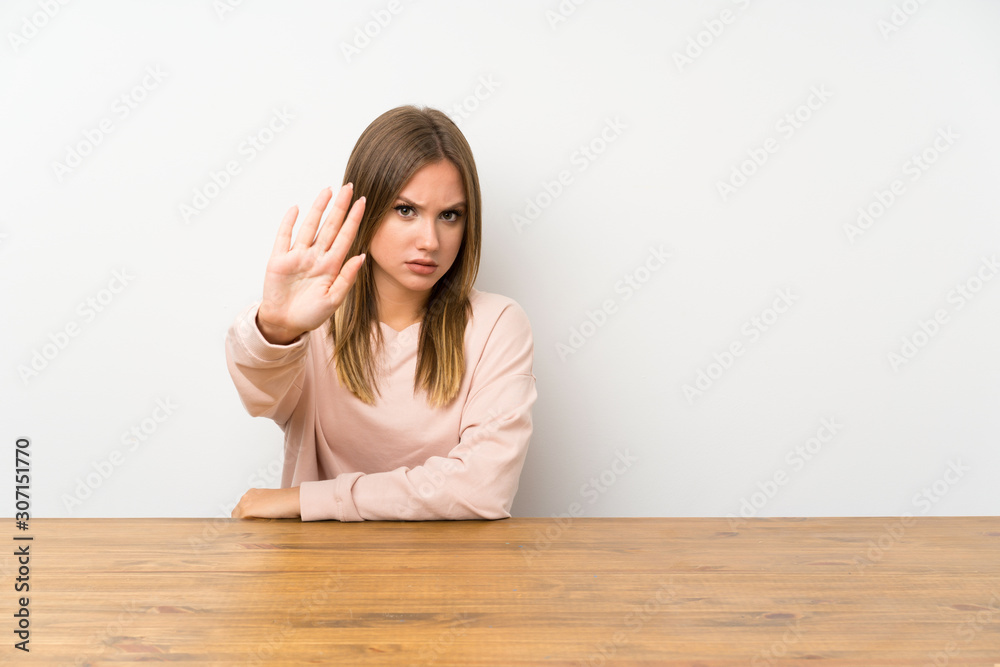 Teenager girl in a table making stop gesture with her hand