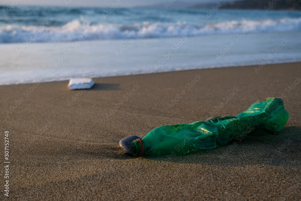 Green Plastic bottle on sea shore,sunset golden light,polluted ecosystem concept Green Plastic bottle on sea shore,sunset golden light,polluted ecosystem concept
