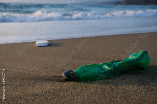 Green Plastic bottle on sea shore,sunset golden light,polluted ecosystem concept