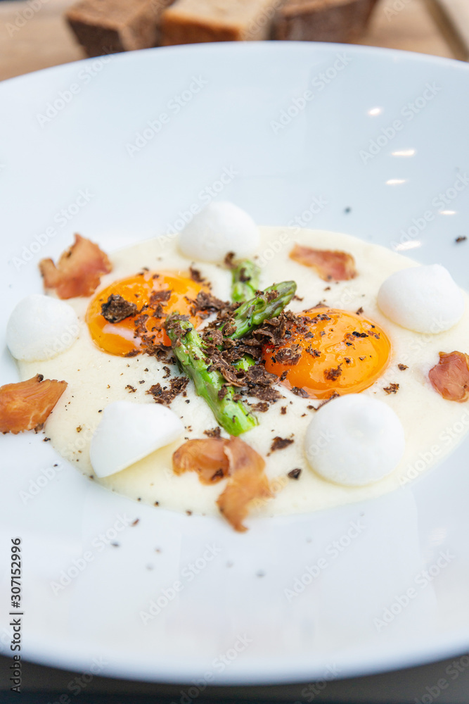 Starter cooked with soft boiled yellow eggs, asparagus, salted meringue and Cretan pork with truffles on top of the dish, served in white plate.