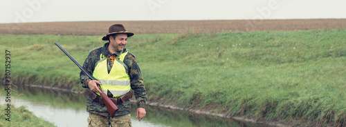 Hunting period, autumn season open. A hunter with a gun in his hands in hunting clothes in the autumn forest in search of a trophy. A man stands with weapons and hunting dogs tracking down the game.