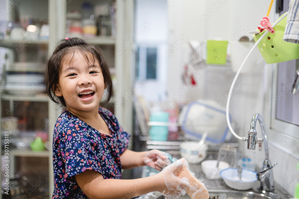 Happy smiley laughing face little cute asian girl washing dishes in kitchen for help her mom.Child development and Executive functions concept. Happy smiley laughing face little cute asian girl washing dishes in kitchen for help her mom.Child development and Executive functions concept.
