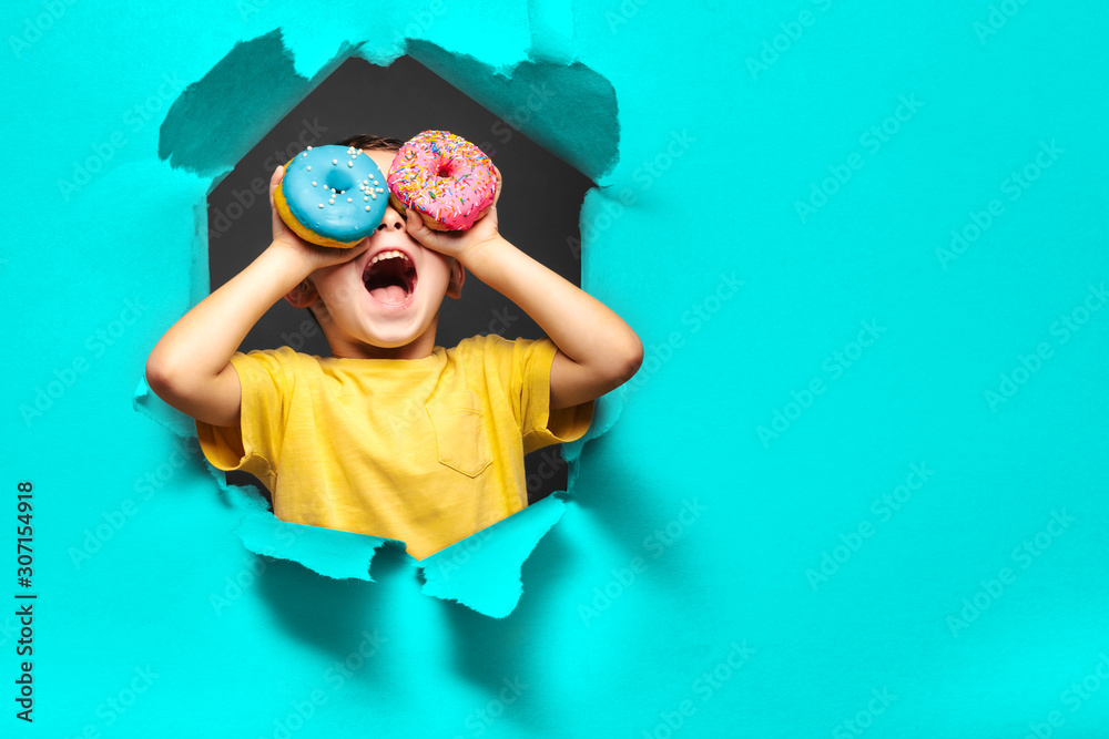 Happy cute boy is having fun played with donuts on black background wall. - obrazy, fototapety, plakaty 
