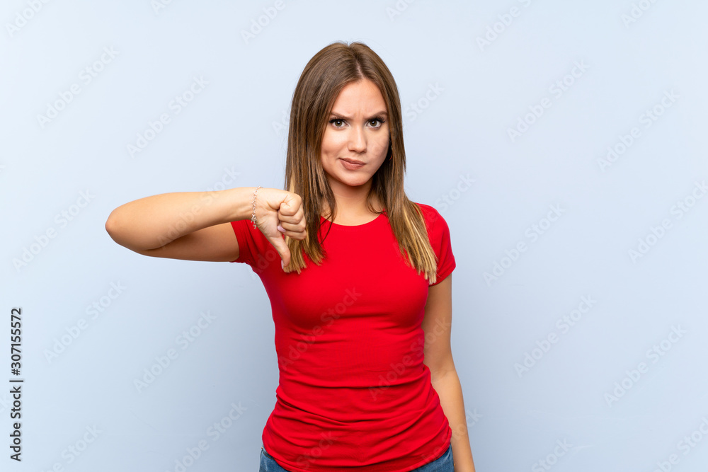 Teenager girl over isolated blue background showing thumb down sign