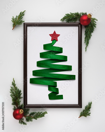 Stylized Christmas tree made from green ribbon with red shiny star and Christmas balls in photo frame on white background. Flat lay, top view, vertical layout