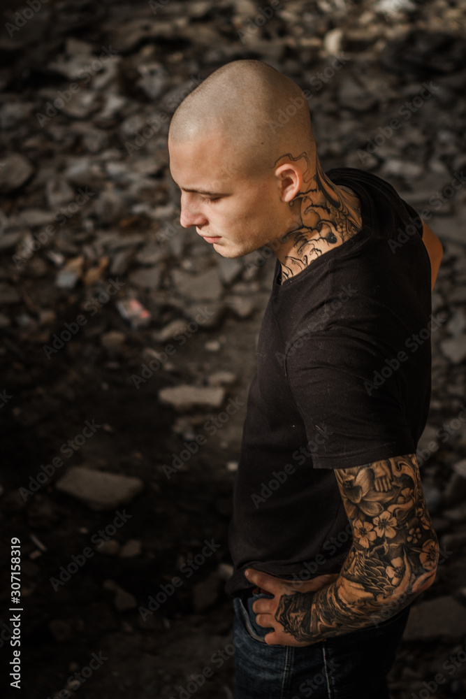 Bald brutal young man with tattoos stuffed on his arms and neck against the  background of