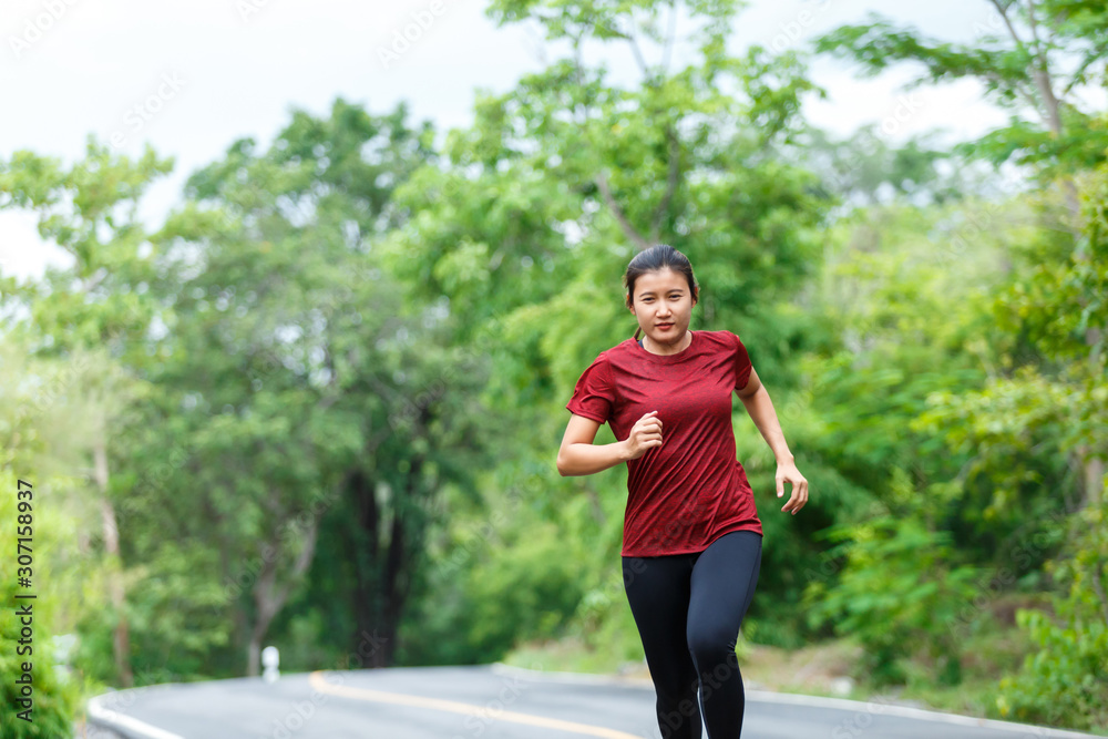 Front of woman runner and runing with full speed at the road surround with green forest.