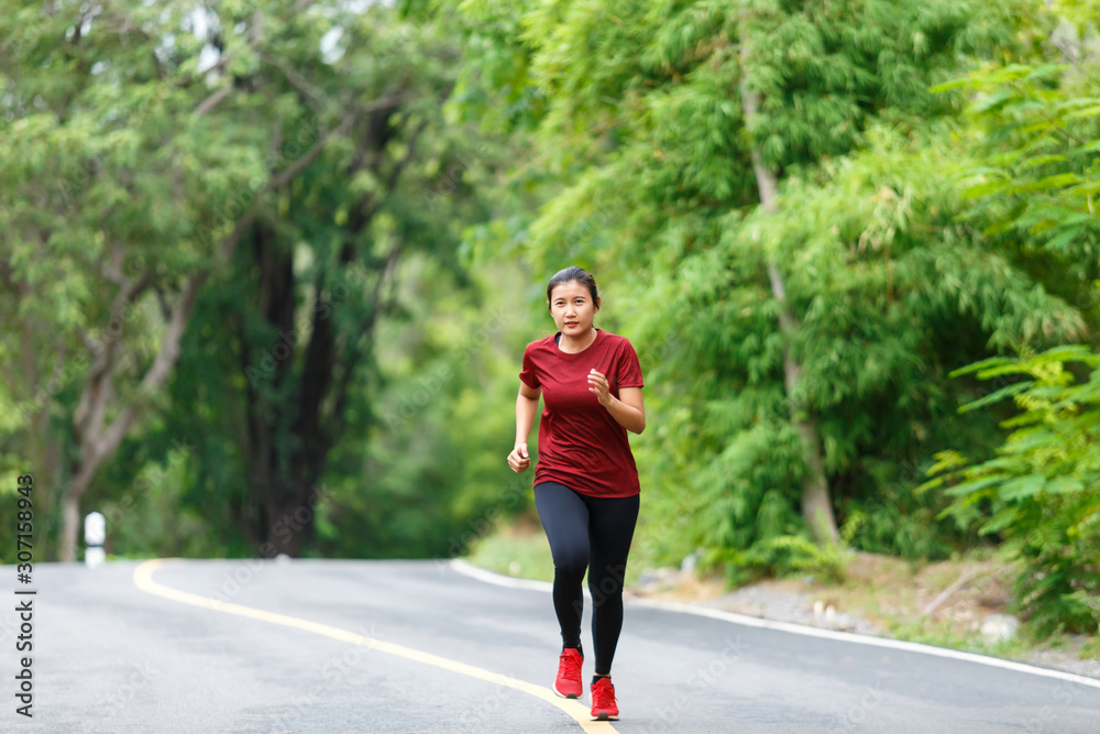 Front of woman runner and runing with full speed at the road surround with green forest.