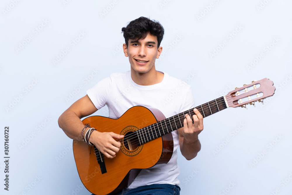 Young Argentinian man with guitar over isolated blue background Young Argentinian man with guitar over isolated blue background