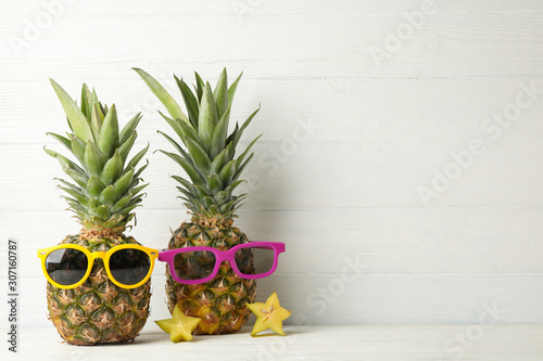 Pineapples with sunglasses on white wooden background, space for text