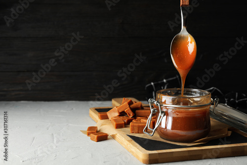 Photos Glass jar with salted caramel and candies on grey background, space for text