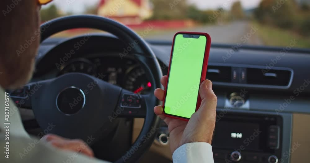 Unrecognizable elderly man hand using chromakey mobile phone with empty green screen in modern car. Scrolling smartphone display closeup. Mockup touchscreen. Male driver internet searching online. Unrecognizable elderly man hand using chromakey mobile phone with empty green screen in modern car. Scrolling smartphone display closeup. Mockup touchscreen. Male driver internet searching online.