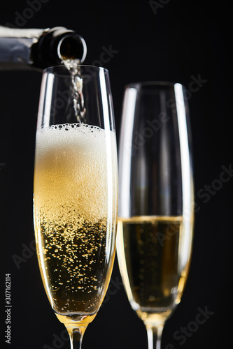 sparkling wine pouring from bottle into glasses for celebrating christmas, isolated on black