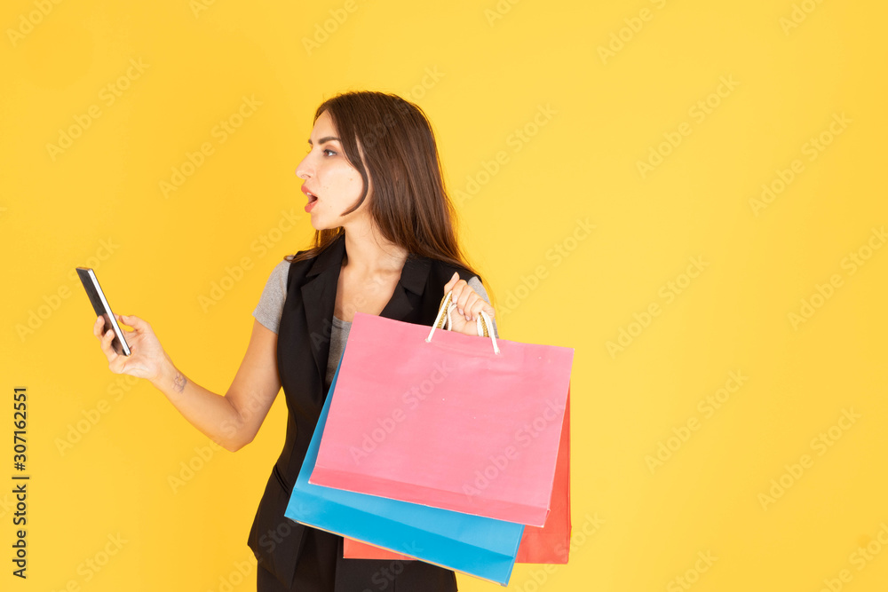 A woman with a phone The other hand is carrying a multicolored shopping bag, leaving space to put text in a yellow background. A woman with a phone The other hand is carrying a multicolored shopping bag, leaving space to put text in a yellow background.