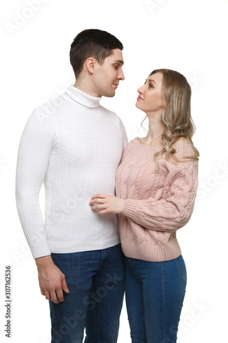 A loving guy and a girl stand in an embrace in casual clothes and look at each other isolated on a white background.