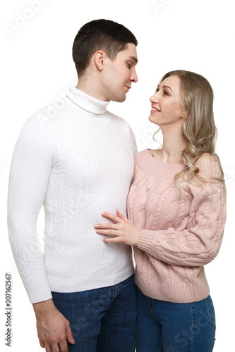 A loving guy and a girl stand in an embrace in casual clothes and look at each other isolated on a white background.