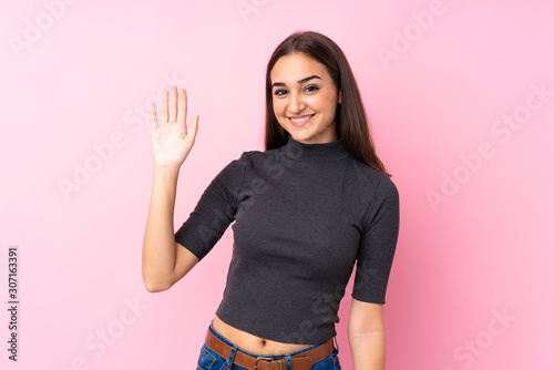 Young girl over isolated pink background saluting with hand with happy expression