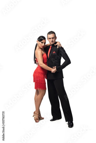stylish couple of dancers looking at camera while performing tango on white background