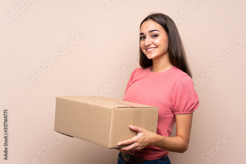 Young woman over isolated background holding a box to move it to another site © luismolinero