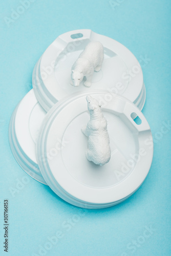 Top view of toy polar bears on plastic coffee lids on blue background, ecological problem concept