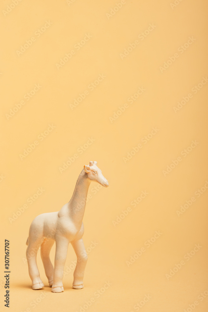 Obraz premium White toy giraffe on yellow background, animal welfare concept