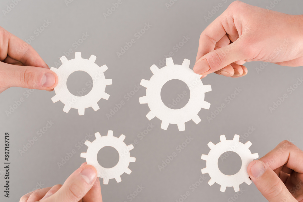cropped view of people holding white gears isolated on grey cropped view of people holding white gears isolated on grey