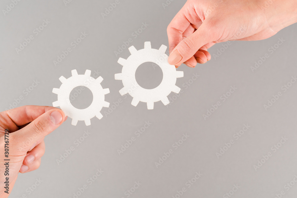 cropped view of people holding white gears isolated on grey cropped view of people holding white gears isolated on grey