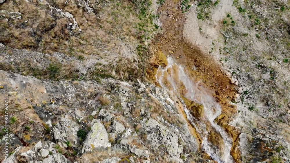 Aerial shooting of a mountain waterfall. Mountain stream flows down from a dry cliff, carries water to variegated stones, washing the rock. Aerial shot taken by drone Aerial shooting of a mountain waterfall. Mountain stream flows down from a dry cliff, carries water to variegated stones, washing the rock. Aerial shot taken by drone
